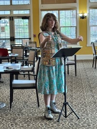 A girl scout conducts a choir class of full of older adult women.