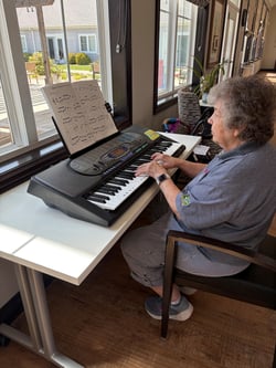 A senior woman practices piano at a senior living community