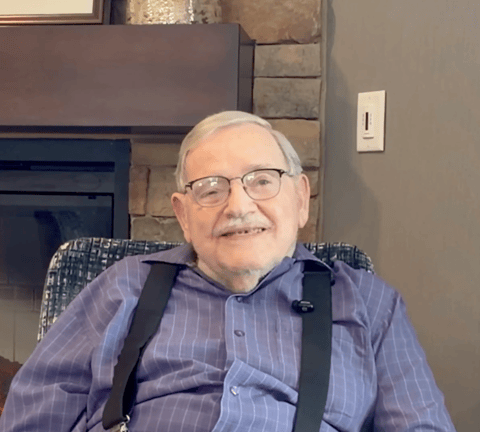A senior living resident sits in a common area of his community and smiles