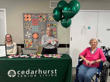 Residents of Cedarhurst Senior Living sit at a booth and give out fabric hearts made by the community's crafting club