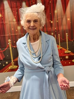 A senior woman walks the red carpet at her senior living community's prom event.