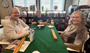 A senior woman plays dominoes with two of her friends, who are also older adults.