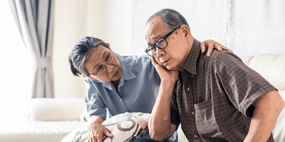 Senior woman comforting her husband while sitting on sofa at home  