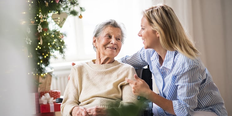 A caregiver comforting an aging parent during the holiday season, surrounded by gifts and a lit tree