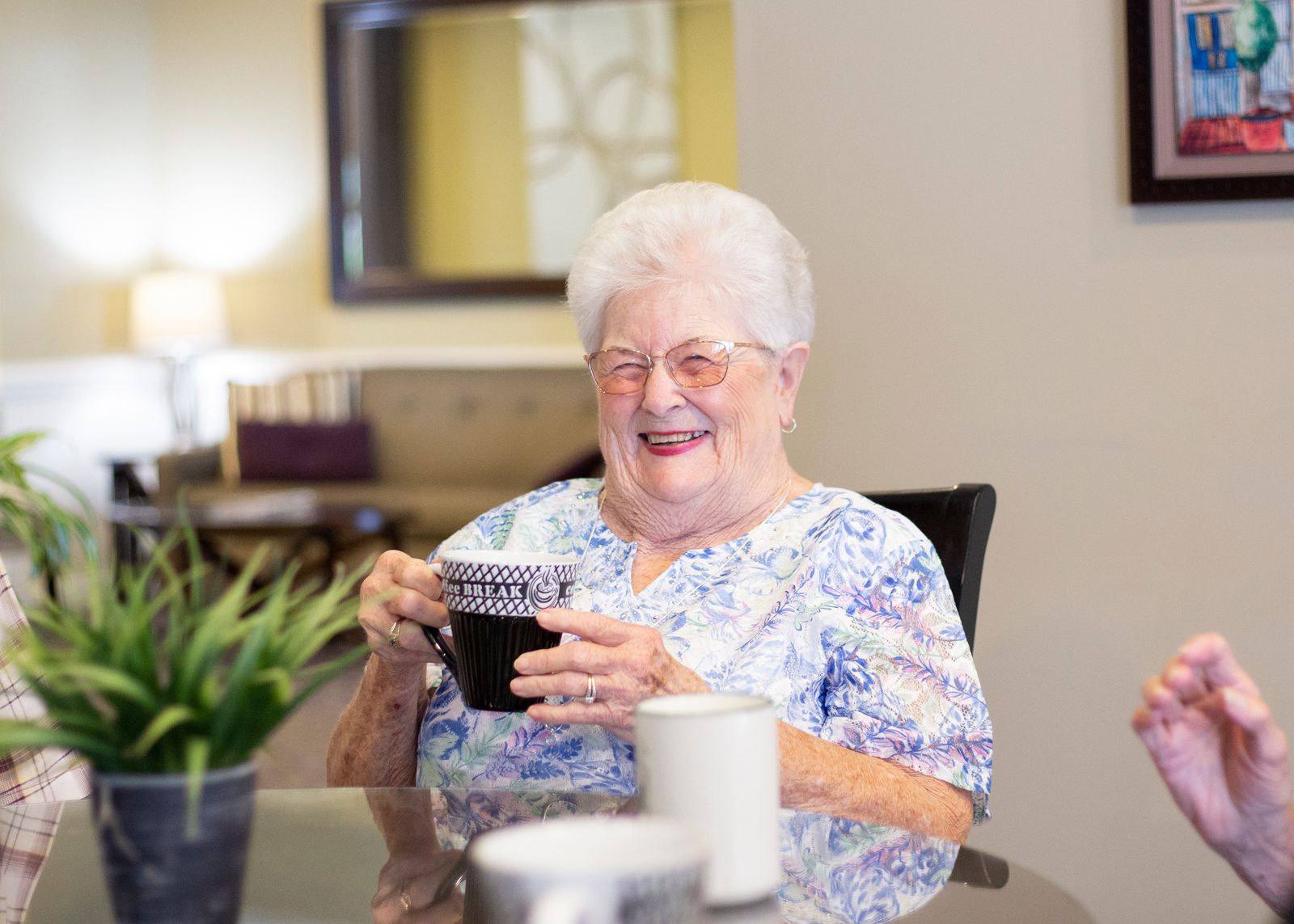 A resident smiling and drinking coffee at a dining room table