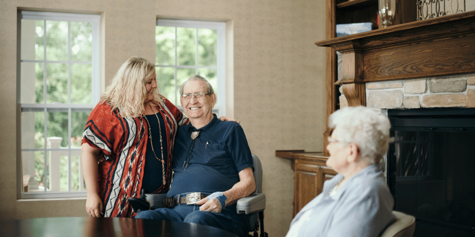 A caregiver stands next to older adults sitting at a table, one of which is in a motorized wheelchair
