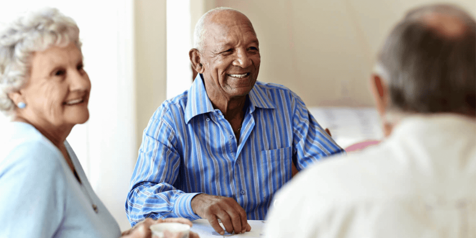 Three assisted living residents chatting at a table while drinking coffee