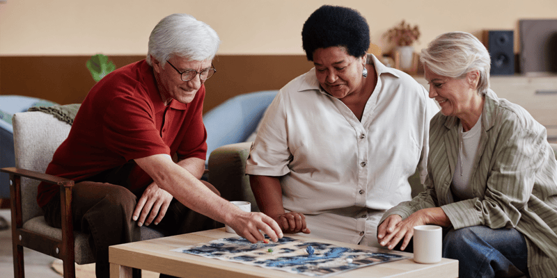  Senior living residents and a team member assembling a puzzle together