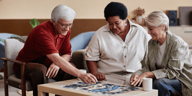 Senior living residents and a team member assembling a puzzle together