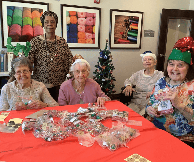 Holidays at Cedarhurst - Senior living community residents gather at a crafting table to assemble holiday gift bags full of sweet treats.