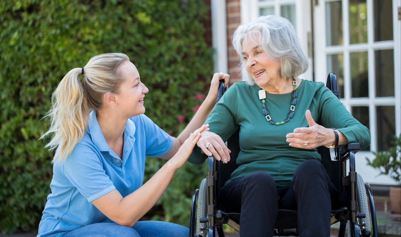 A team member kneeling to chat with a senior resident in a wheelchair