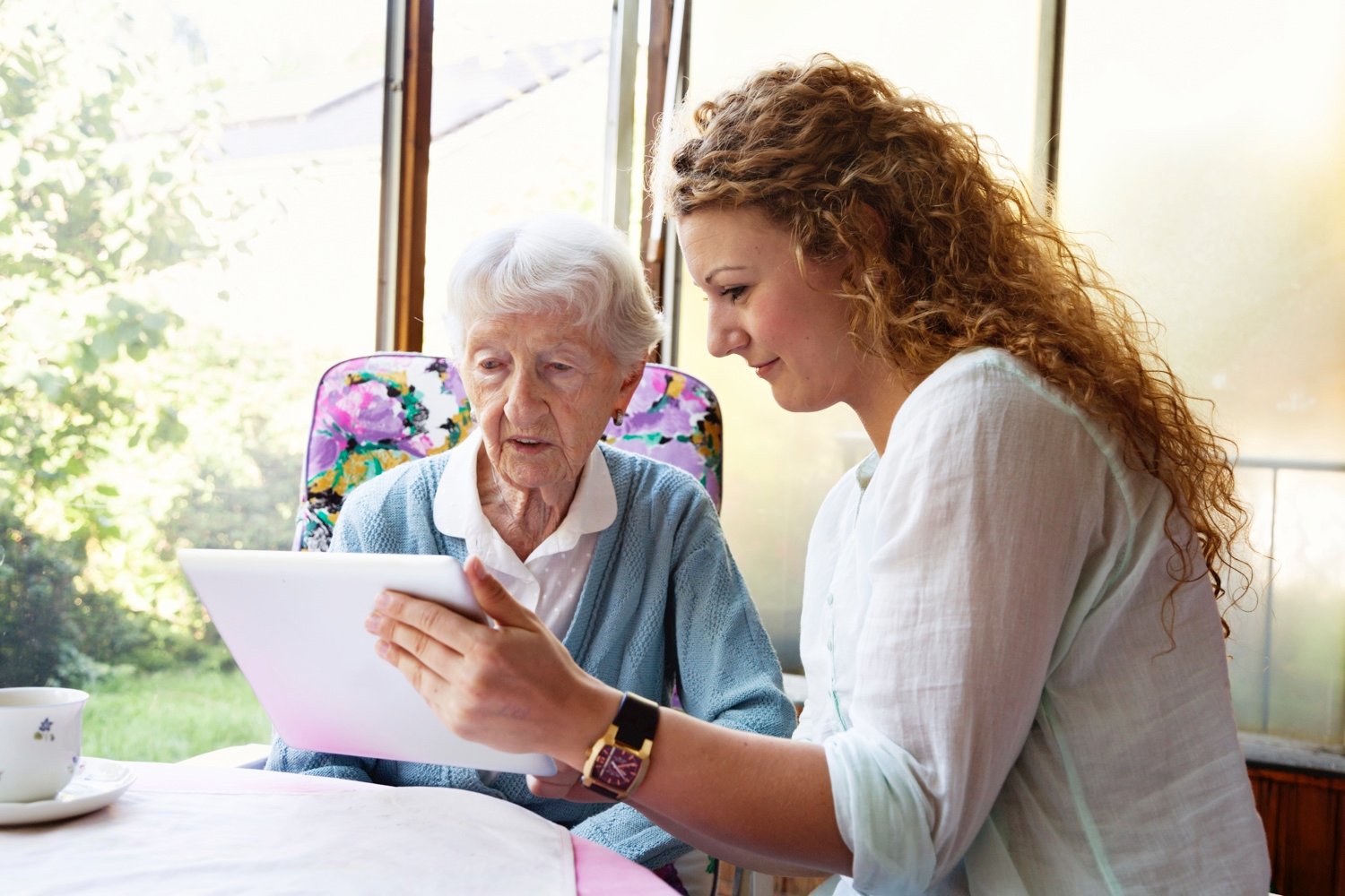 A staff member holding a tablet and reading with a seated senior woman