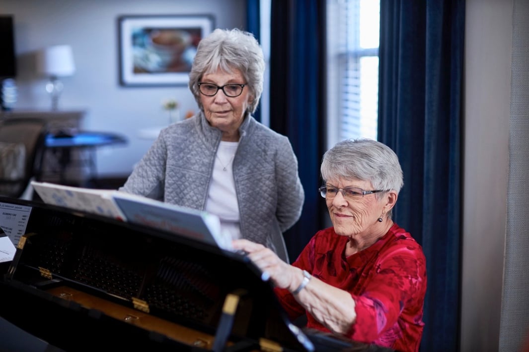 Two women at a piano, one playing and one singing