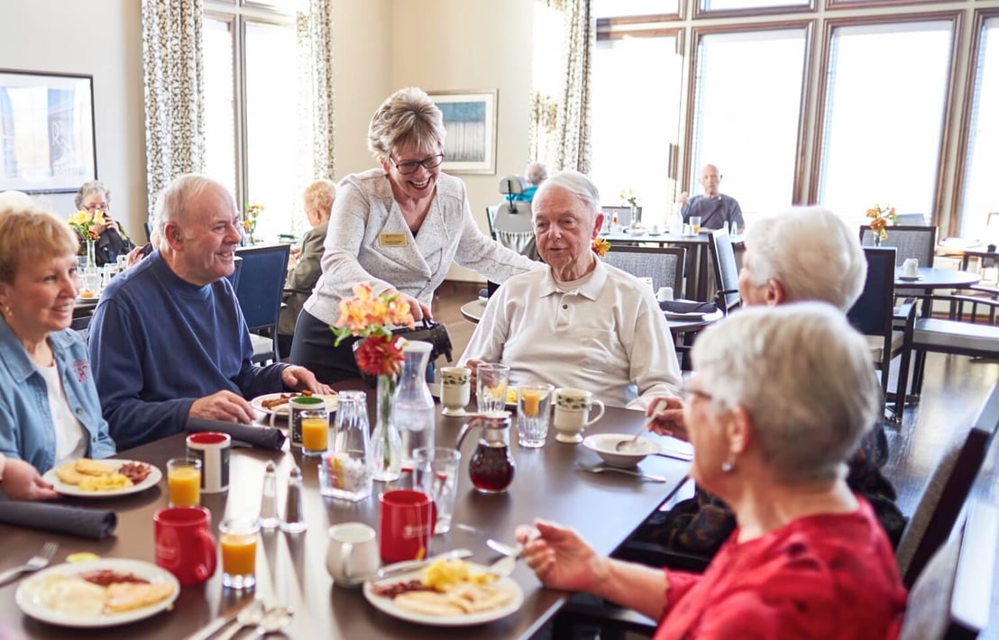 A team member serving coffee to a group of senior residents eating breakfast in the community restaurant