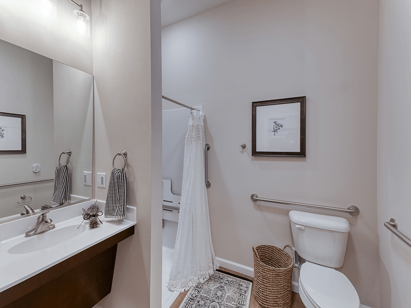 An accessible bathroom in a senior apartment at Cedarhurst of Arnold, featuring safety rails and a roll-in shower