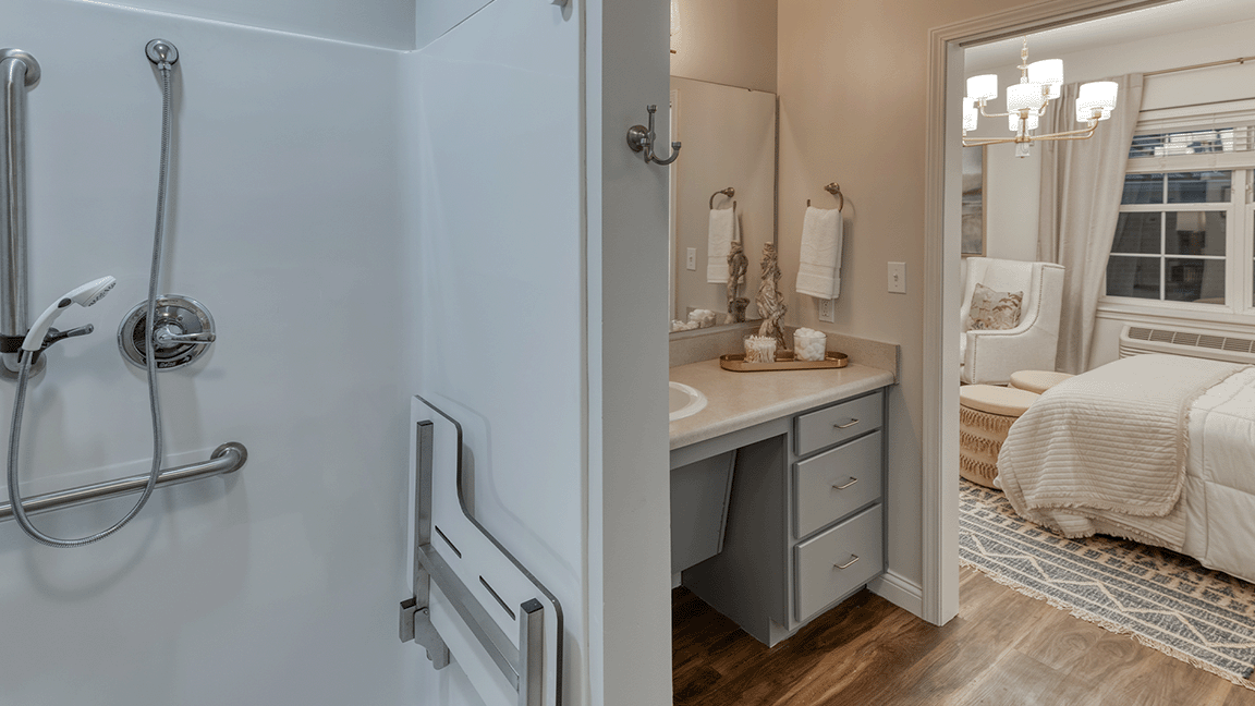 An accessible bathroom in a senior apartment at Cedarhurst of Beaumont, featuring safety rails and a roll-in shower.