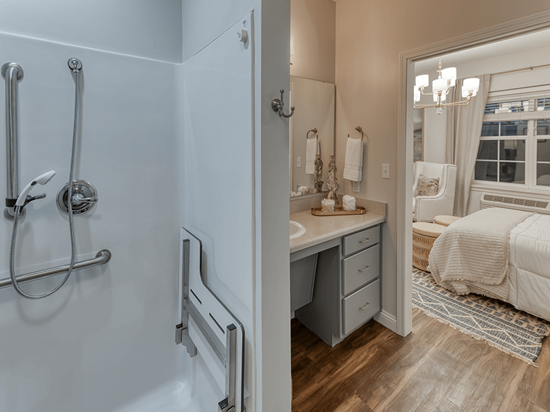 An accessible bathroom in a senior apartment at Cedarhurst of Beaumont, featuring safety rails and a roll-in shower.
