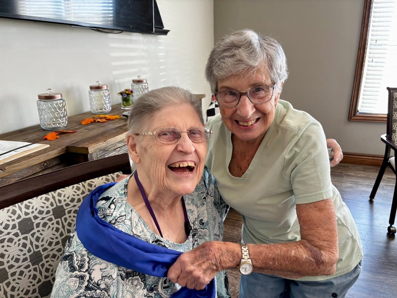 Two friends laughing together in a cozy common area at Cedarhurst of Bethalto senior living community
