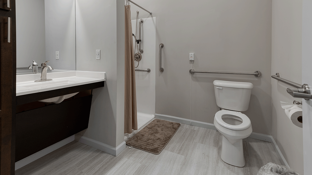An accessible bathroom in a senior apartment at Cedarhurst of Blue Springs, featuring safety rails and a roll-in shower.