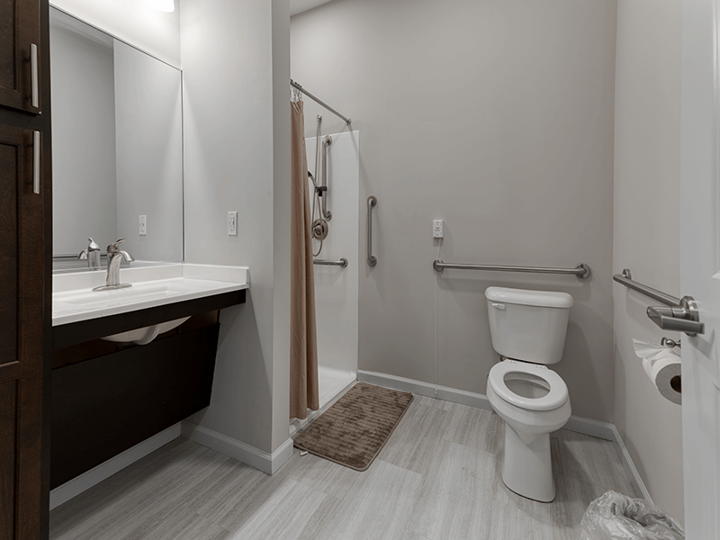 An accessible bathroom in a senior apartment at Cedarhurst of Blue Springs, featuring safety rails and a roll-in shower.