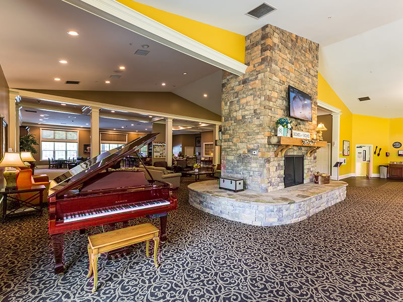 A common area at Cedarhurst of Canton that offers seating around a fireplace and a piano for entertaining.
