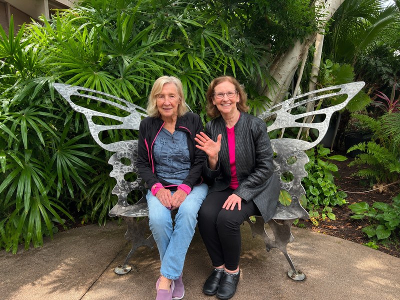 enior living residents posing on a butterfly bench during a garden outing.