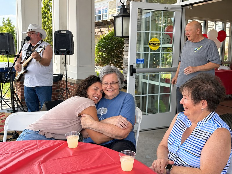 Assisted living resident sharing a warm hug during a live music event on the patio.