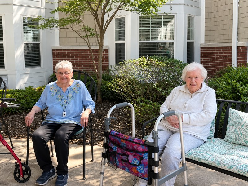 Two assisted living residents relaxing together in a landscaped courtyard.