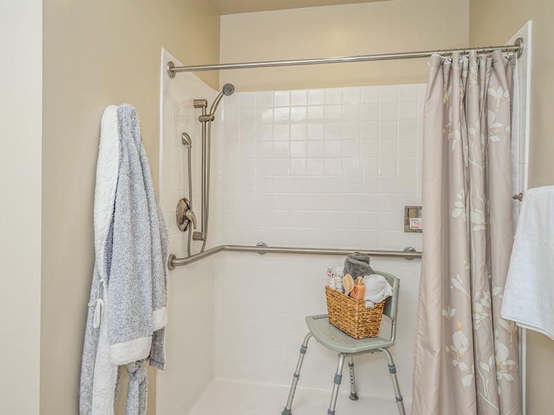 An accessible bathroom in a senior apartment at Cedarhurst of East Louisville, featuring safety rails and a roll-in shower