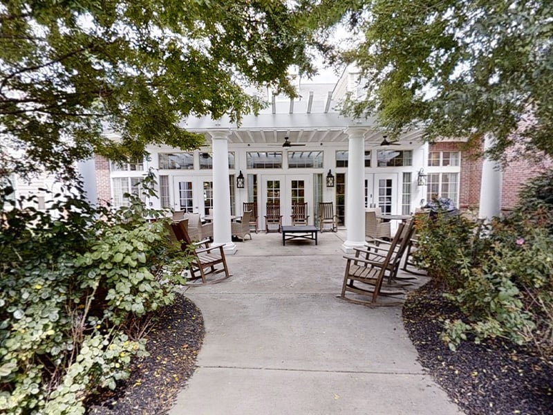 An inviting outdoor area at Cedarhurst of Eat Loisville, showing lush green spaces, paved paths, comfortable seating, and a pergola