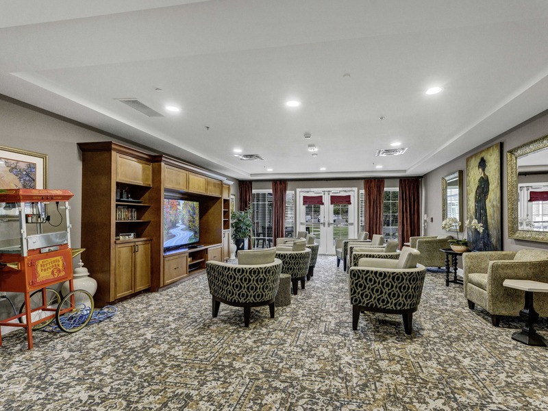 Movie theater with a large TV, comfortable swivel chairs, and a popcorn machine at Cedarhurst of East Louisville assisted living community