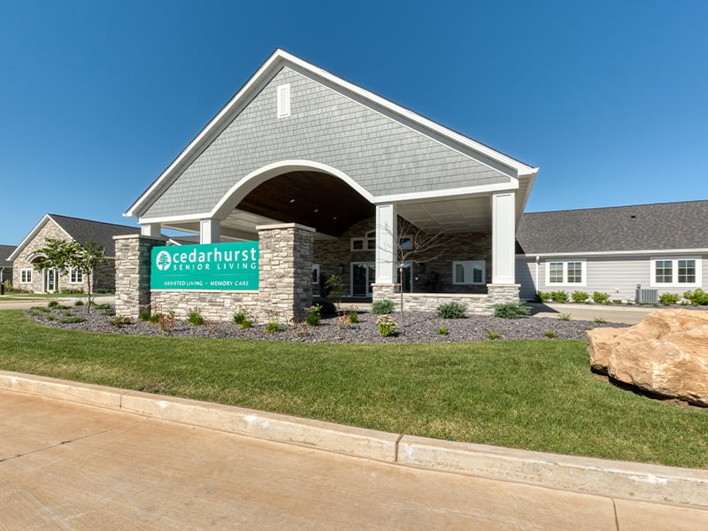 An inviting view of the Cedarhurst of Farmington senior living community from the outside, complete with the main building and its distinctive sign