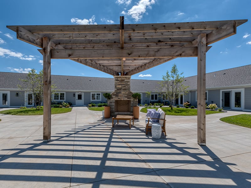 An inviting outdoor patio space with a wooden pergola and fireplace at the Cedarhurst of Farmington senior living community