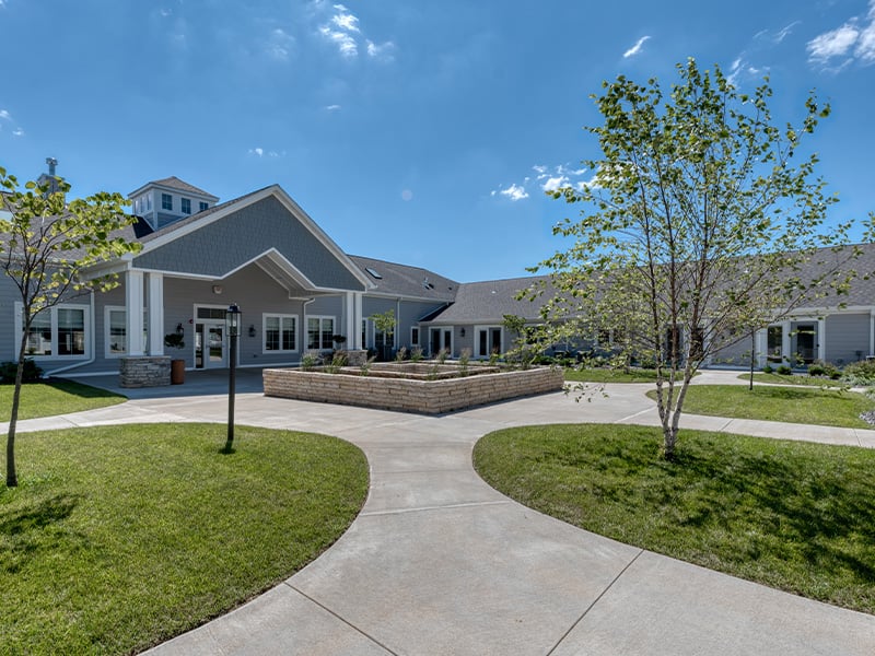 Outdoor green space at Cedarhurst of Farmington with paved walking paths and raised garden beds