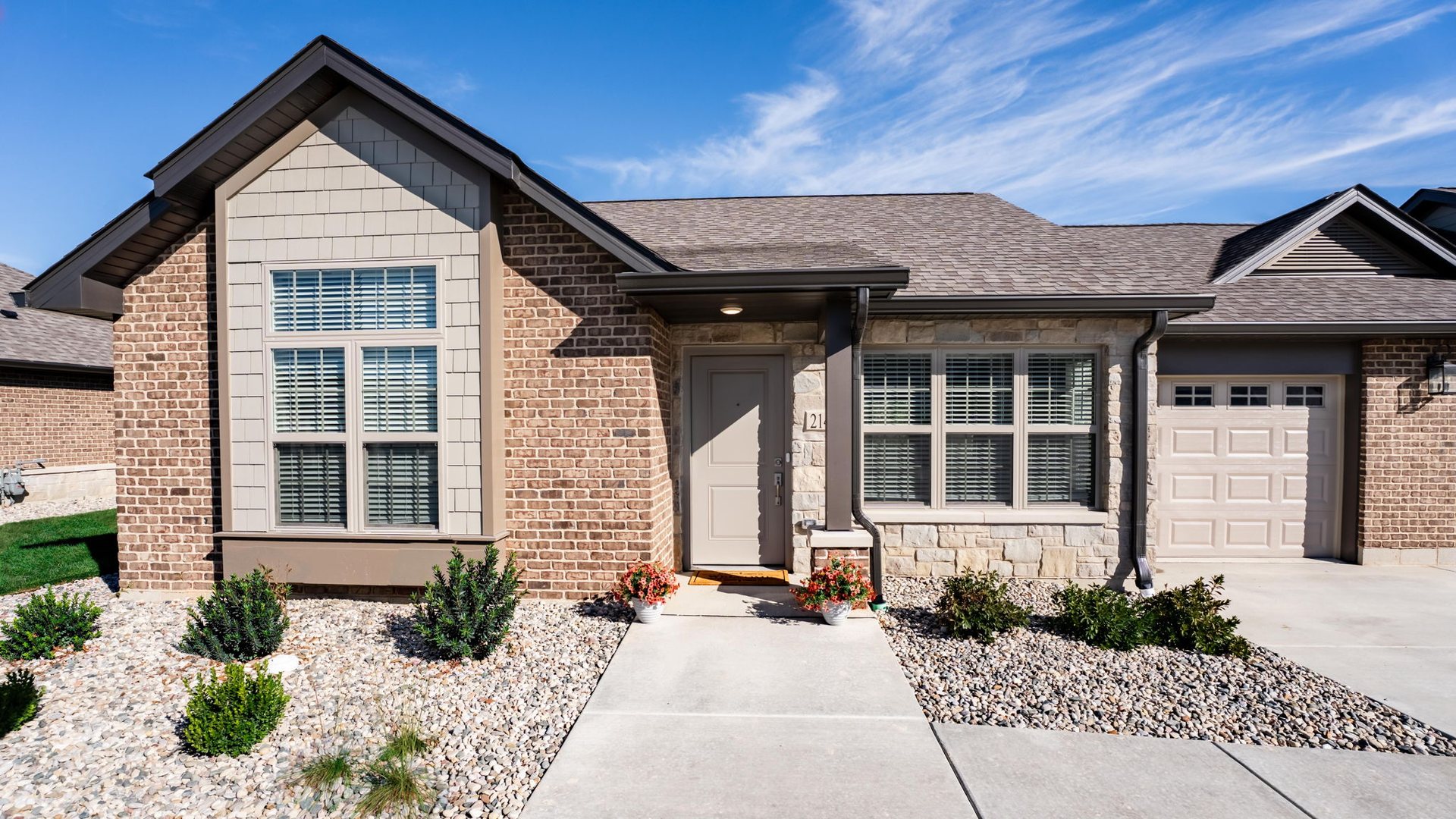 Front of a brick and stone cottage for independent living at Cedarhurst Cottages at Cedarhurst of Frankfort, with a covered entry, landscaped beds, and an attached garage