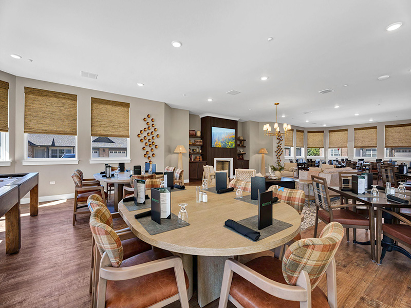 Interior of the Cedarhurst of Frankfort clubhouse with a lounge seating area, round coffee table, chandelier, and dining tables in the background
