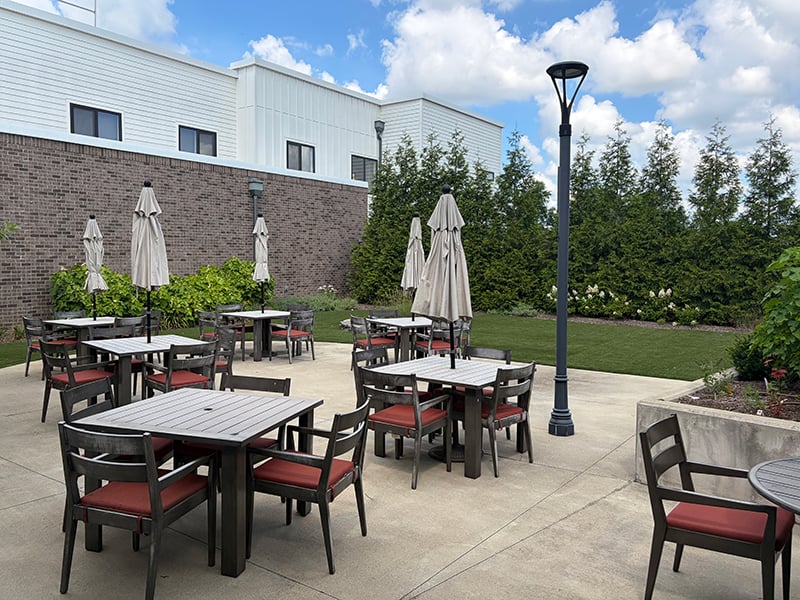 An inviting outdoor area at Cedarhurst of Hamburg, showing lush green spaces, paved paths, a pergola, and a covered patio.