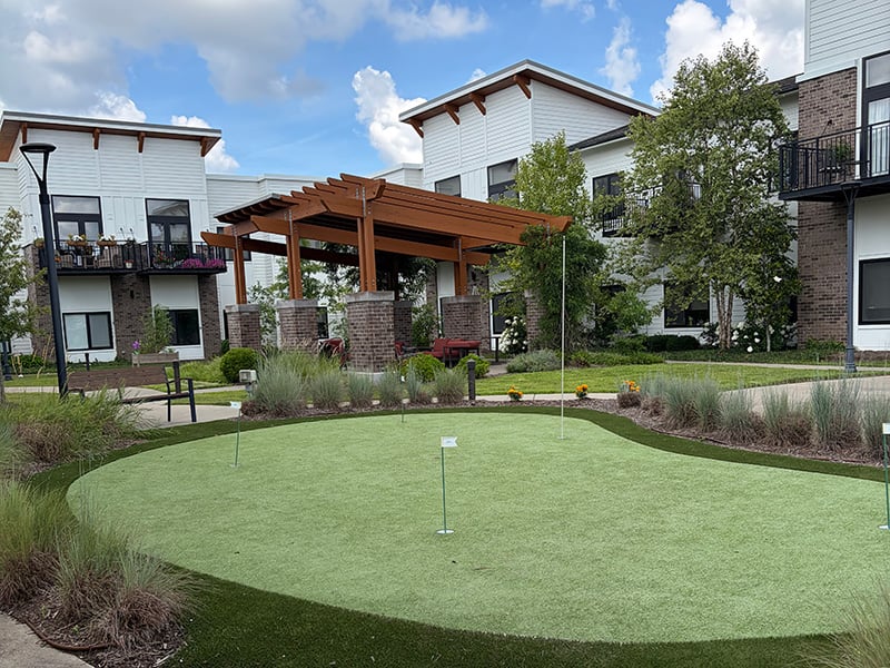 The outdoor putting green at Cedarhurst of Hamburg featuring an adjacent shaded pergola and modern, comfortable seating for residents.