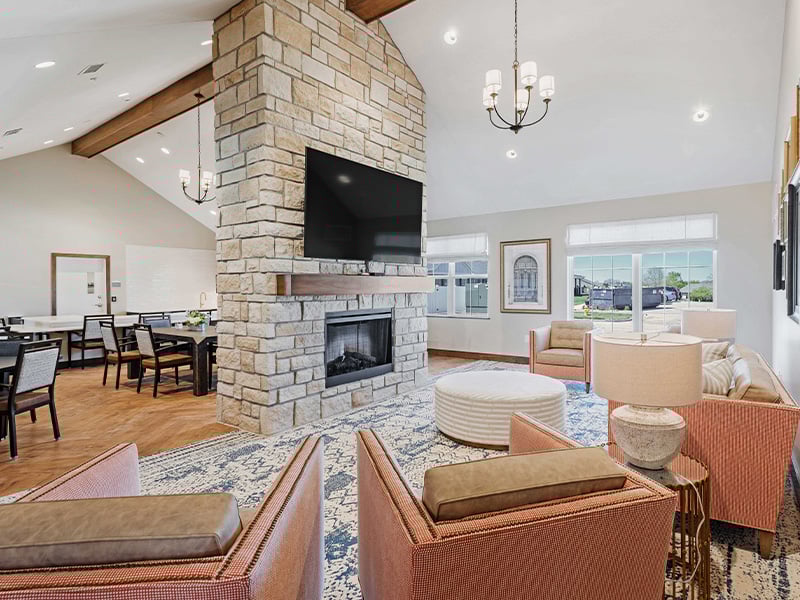 A beautifully designed common area at Cedarhurst of Lawrence, offering a welcoming space for residents to connect, featuring comfortable seating, a fireplace, and a television
