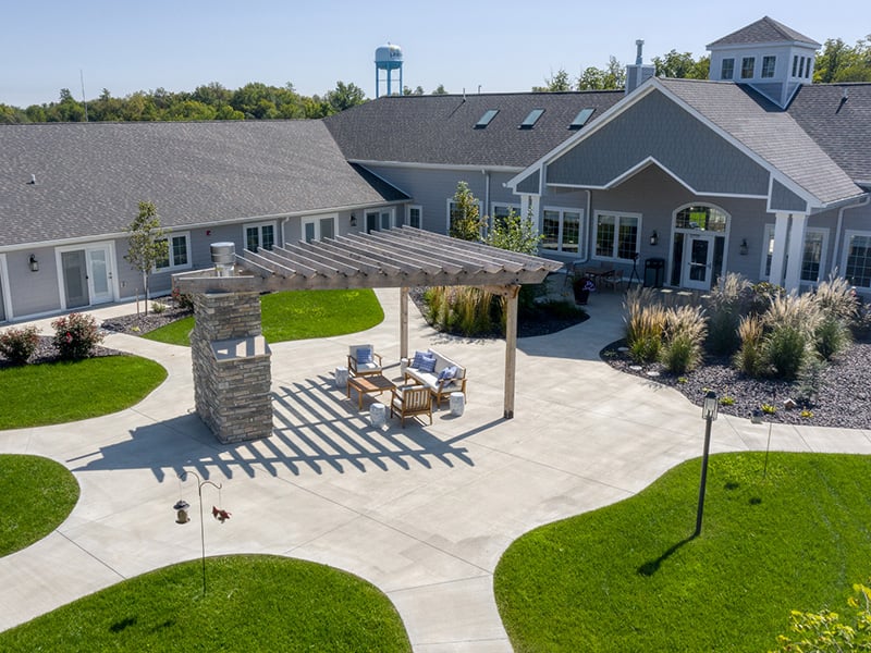 An inviting outdoor area at Cedarhurst of Lebanon, showing lush green spaces, paved paths, a pergola, and a covered patio.