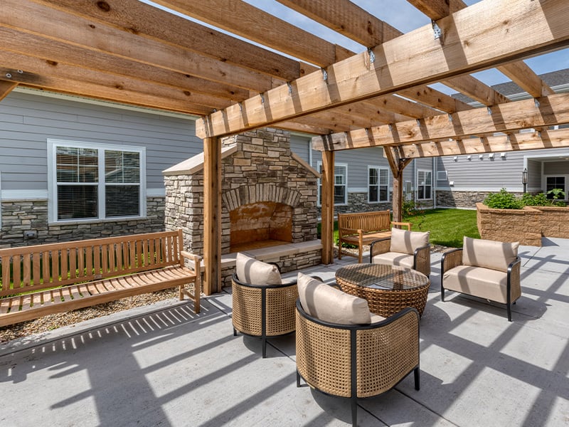 An inviting outdoor patio space with a wooden pergola with fireplace at Cedarhurst of McHenry senior living community.