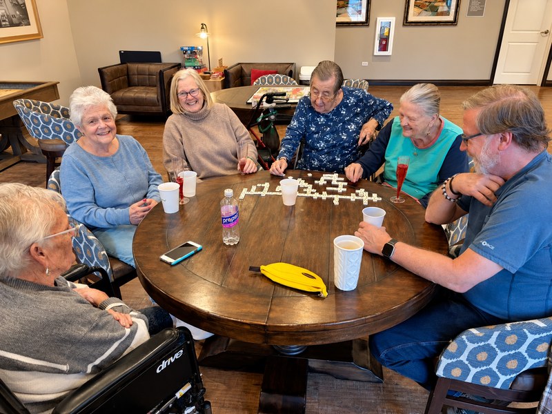 Senior living residents playing a game of dominoes together around a table.
