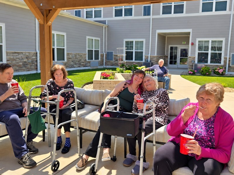 Senior living community residents enjoying cold treats together under a shaded outdoor pavilion.