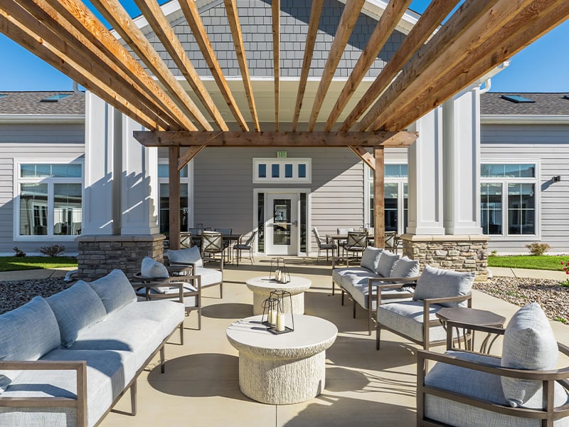 An inviting outdoor area at Cedarhurst of Nicholasville, showing lush green spaces, paved paths, comrtable seating, a pergola, and a covered patio.