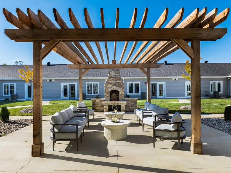 An inviting outdoor patio space with a wooden pergola with fireplace at Cedarhurst of Nicholasville senior living community.