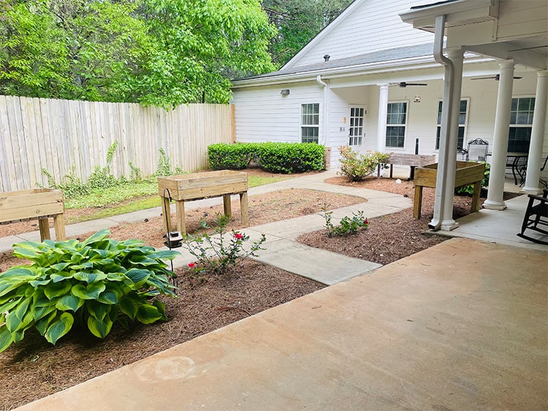 Outdoor green space at Cedarhurst of Oakwood with paved walking paths, covered seating, and raised garden beds