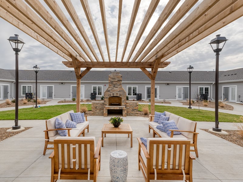 An inviting outdoor patio space with a wooden pergola with fireplace at Cedarhurst of Owensboro senior living community.