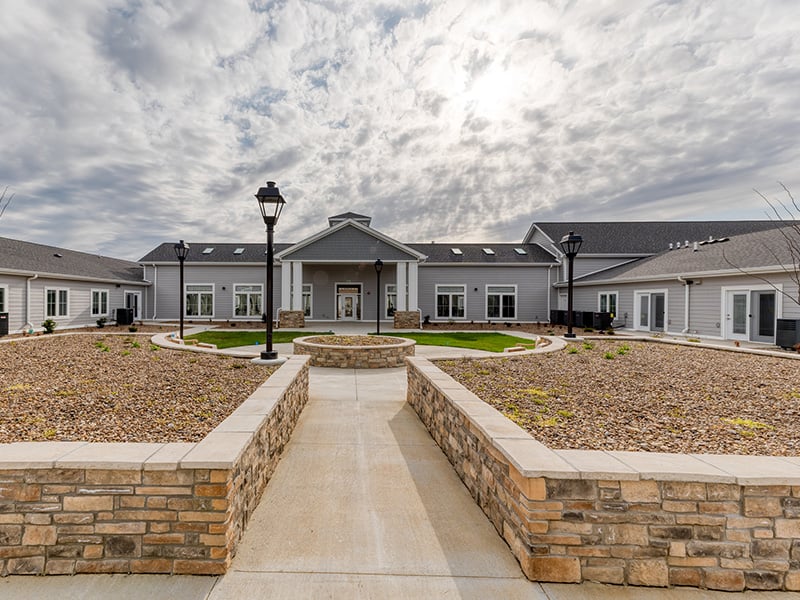 Outdoor green space at Cedarhurst of Owensboro with paved walking paths and raised garden beds.