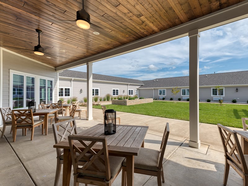 An inviting outdoor area at Cedarhurst of Springfield, IL, showing lush green spaces, paved paths, comfortable seating, and a covered patio