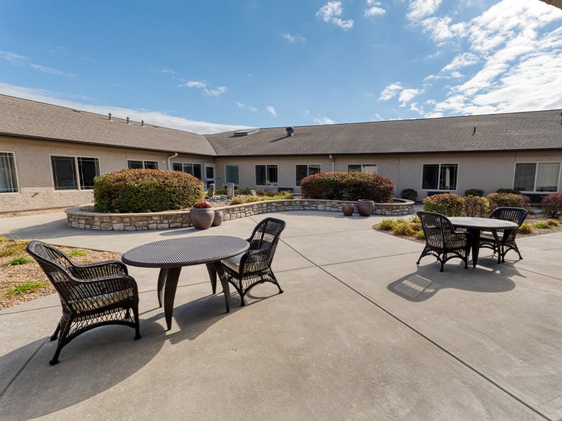 An inviting outdoor area at Cedarhurst of Springfield, MO, showing lush green spaces, paved paths, and comfortable seating